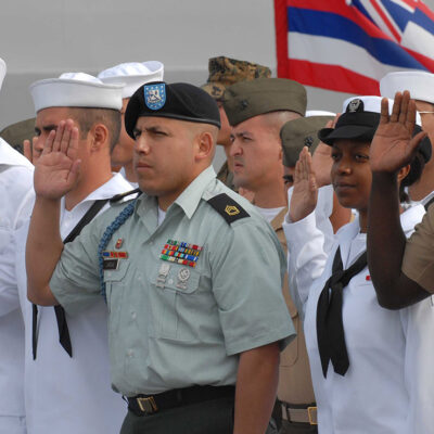 Sailors and Marines with right hands raised taking the oath of citizenship aboard the USS Cleveland.