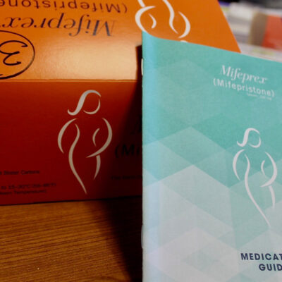 An orange Mifepristone box and blue medication guide.