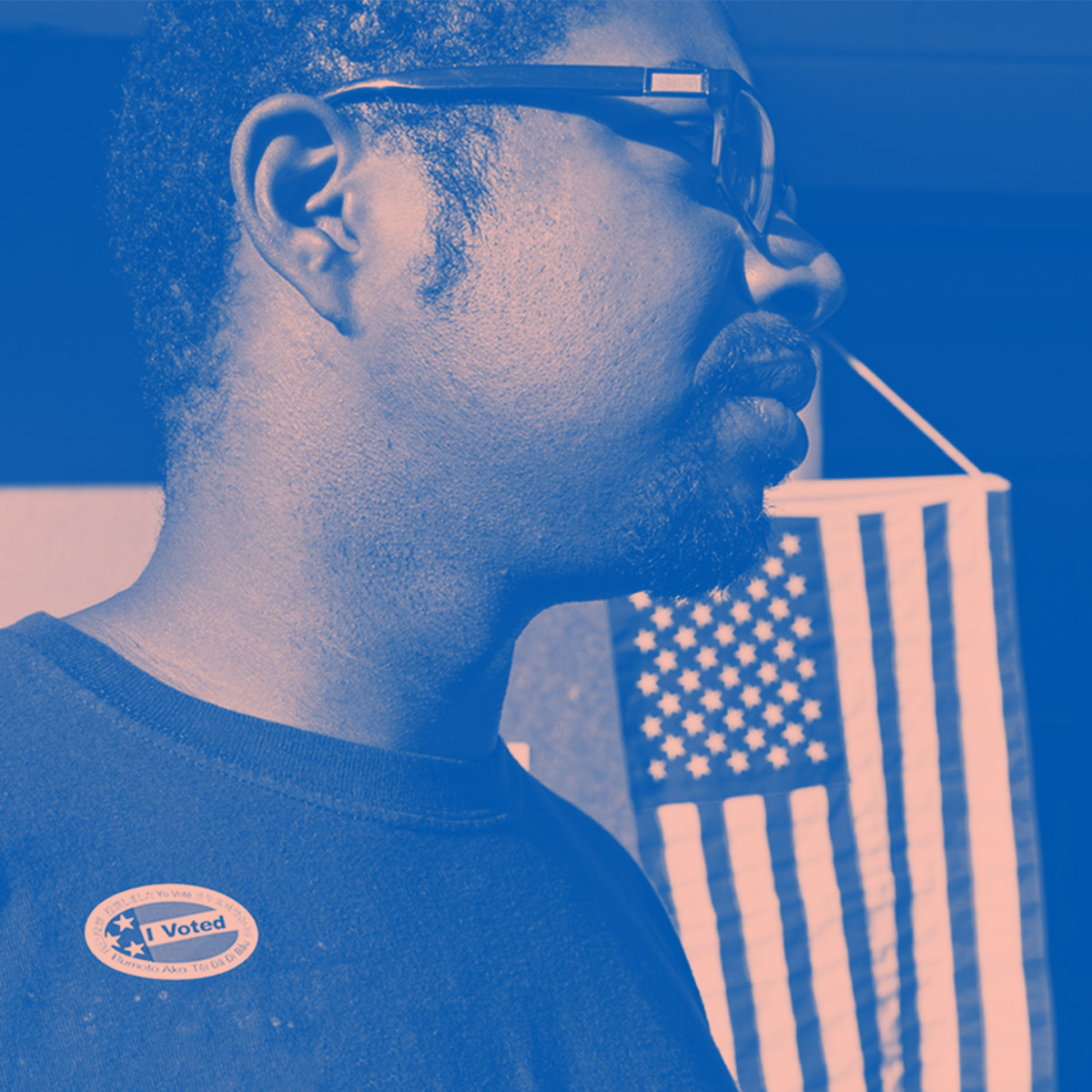 A man wears an "I Voted" stick with the American flag hanging in the background. Image tinted blue and pink.