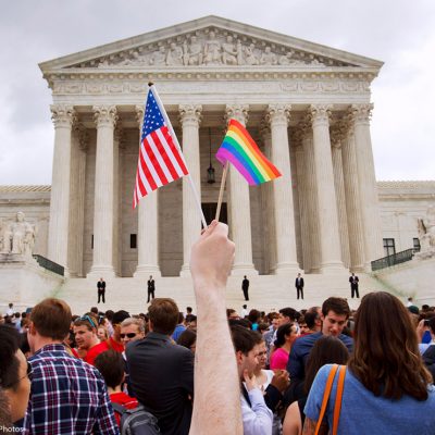 Person holds a mini-American flag and mini-rainbow flag outside of the Supreme Court.