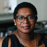 A headshot of Ashley C. Ford, a black woman with short hair and glasses.