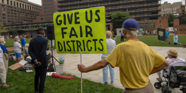 The back of a demonstrator holding a sign that says "Give Us Fair Districts."