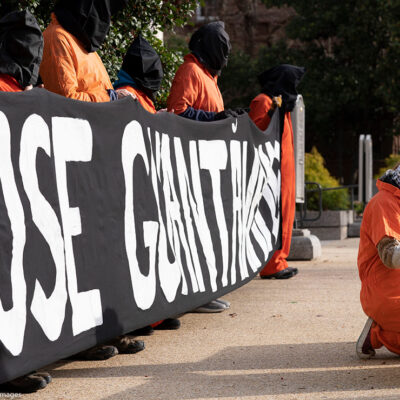 Demonstrators dressed like Guantanamo Bay detainees, hold a banner asking to close Guantanamo.