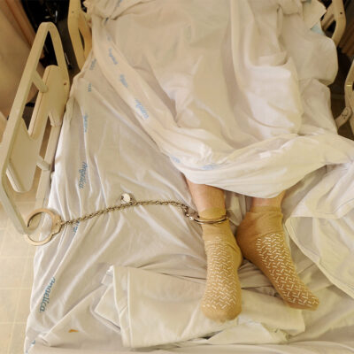 A prisoner lying in a hospital bed with one leg shackled to the bed rail in California medical facility.