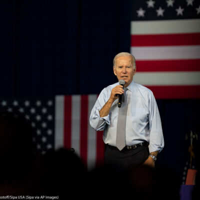 Joe Biden speaking in front of several American flags.