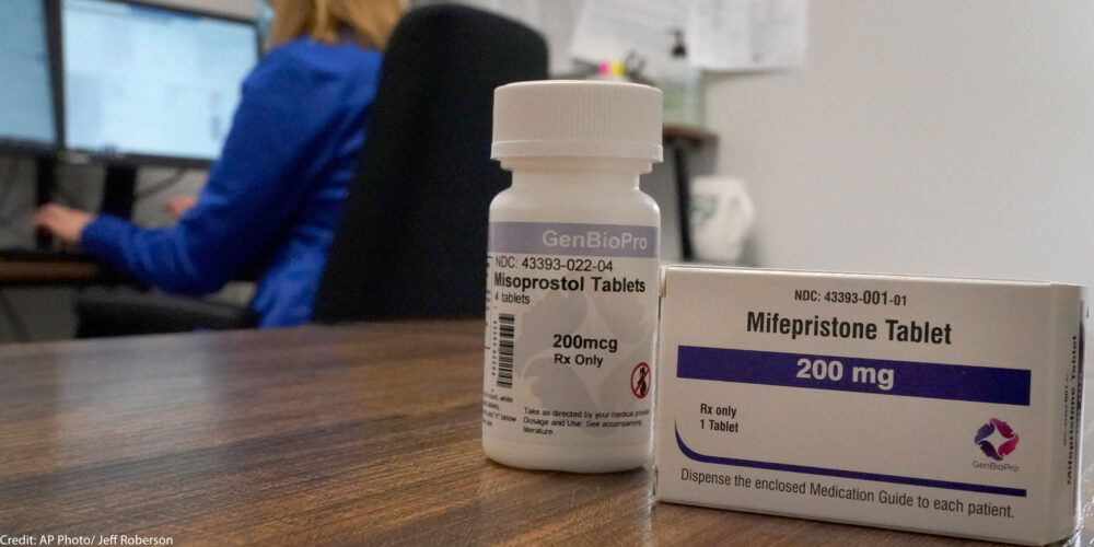 A box of the drug mifepristone pictured in front of a women on a computer.