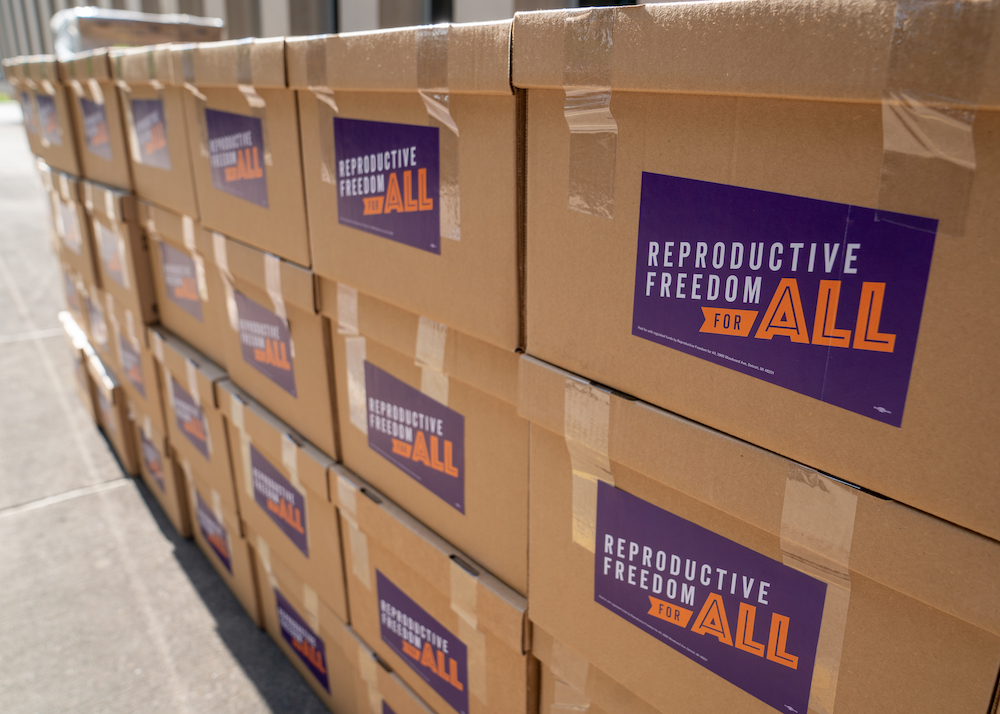 A stack of boxes that say Reproductive Freedom For All filled with signatures.