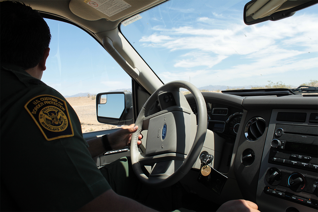 A Customs and Border Protection agent in his car looks out the driver side window.