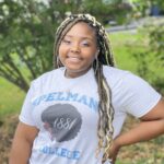Amara Harris smiling, standing in front of a tree. She is wearing a Spelman College t-shirt and hoop earrings.