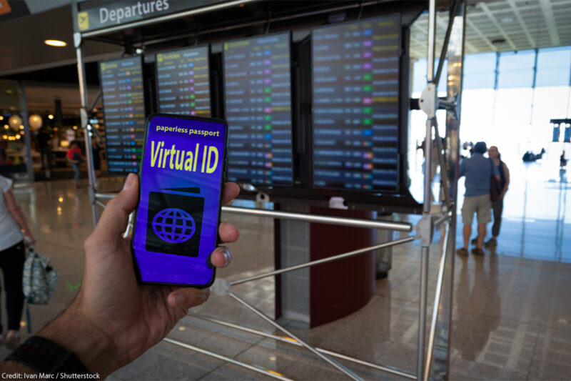 Hand holding a paperless passport virtual ID on smartphone screen with airport timetables as background.