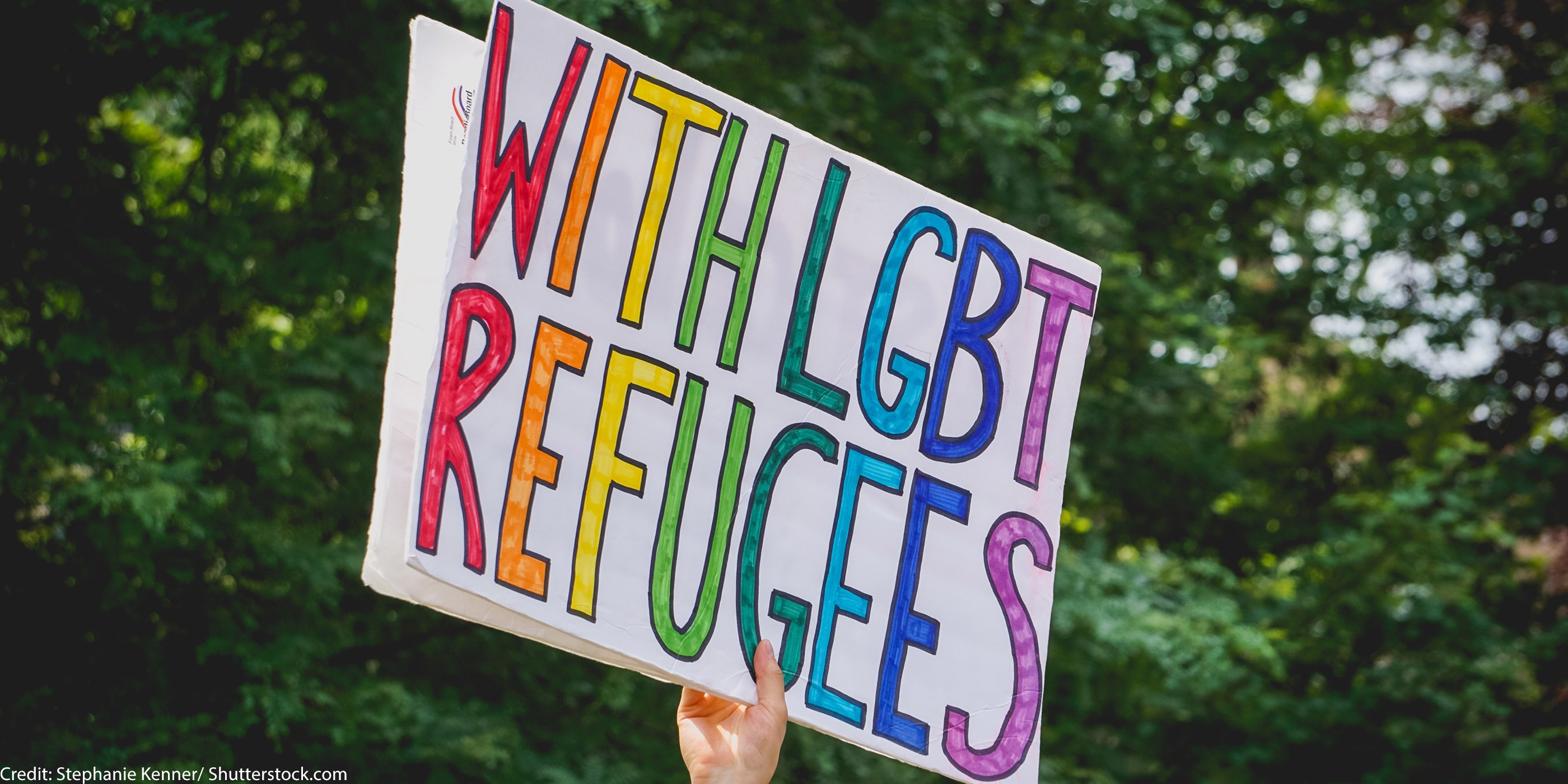 An individual holding a sign that says "With LGBT Refugees."