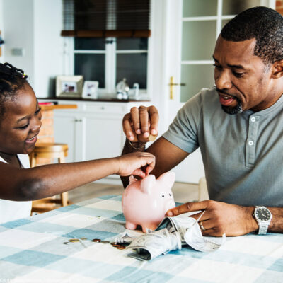 Black father and daughter saving money to piggy bank